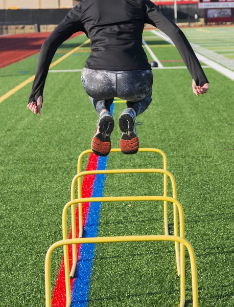 Female athlete jumping over training hurdles from behind — Stock Photo, Image