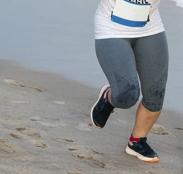 Corredor em leggings cinzentos pela água na praia — Fotografia de Stock