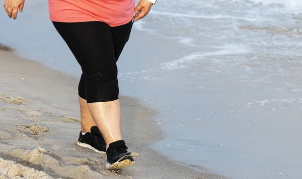 Pernas de uma pessoa pesada andando para o exercício na areia pelo w — Fotografia de Stock