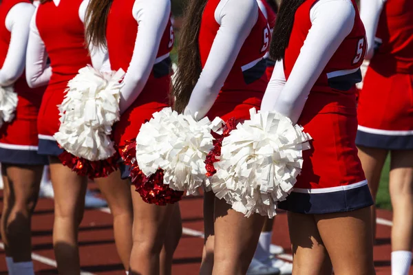 Rear view of cheerleaders with their red and white pom poms behi