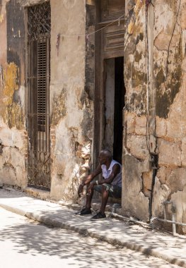 Cuban man sitting in the shade of his doorway smoking a cigarett