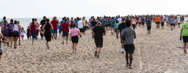 Rear view of hundres of runners on the beach