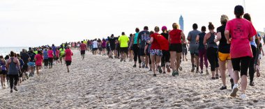 Rear view of runners and walkers on the sand at the beach