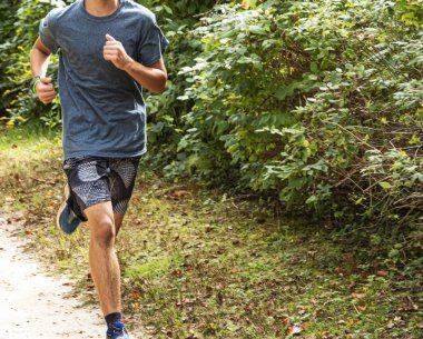 Uzun çalıların yanında toprak yolda koşan bir koşucu