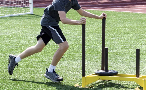 Sportler schiebt Schlitten mit Gewicht auf Rasenplatz — Stockfoto