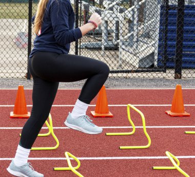 Koşucu sarı mini engelleri ve turuncu konileri aşıyor.