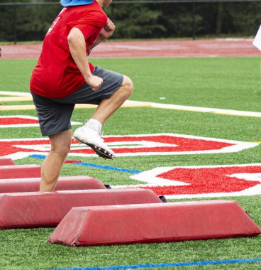 Yeşil bir çim tarlasında yaz kampı sırasında bir lise futbolcusu kırmızı bariyerleri aşıyor..