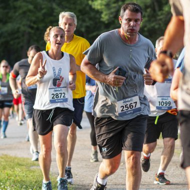 West Babylon, New York, USA - 8 July 2019: Runners racing a 5K around Belmont Lake with one runner giving a peace sign and wearing a shirt with a peace sign.