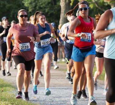 Kuzey Babylon, New York, ABD - 8 Temmuz 2019: Belmont Gölü Parkı etrafında kalabalık bir 5K 'da yarışan bir bayan koşucu saatini kontrol ediyor