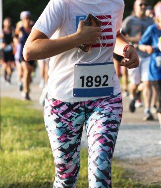 ABD 'deki Belmont Gölü Parkı' nda bir yarış sırasında cep telefonu taşıyan ve çimlerin üzerinde renkli tayt giyen bir koşucunun dikey görüntüsü.