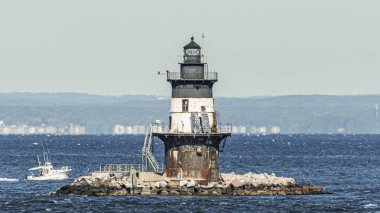 Orient Point deniz feneri. Arka planda, dalgalı sularda yüzen bir balıkçı teknesi var..