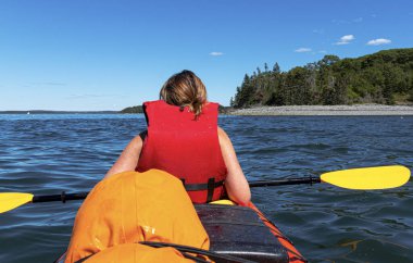 Frenchmans Bay Bar Harbor Maine 'de kayak yapan bir bayanın arkasındakinden, arka plandaki kirpi adalarından birine yakın durun..