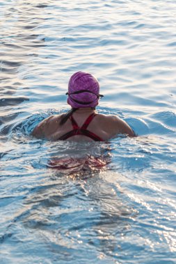 Dışarıdaki havuzda yüzen pembe şapkalı bir kadının arka görüntüsü..