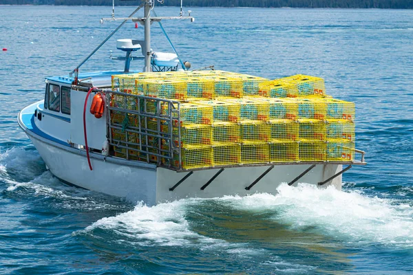 A fishing boat in the waters of Bar Harbor Maine has yellow lobster traps staked four high on a full boat ready to be placed in the water.