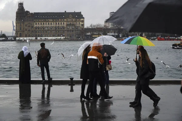 イスタンブール トルコ 2018 イスタンブール カディコイの海辺で雨の日 傘を持って歩いている人もいれば ハイダルパサ駅の風景を見ている人もいる ロイヤリティフリーのストック写真