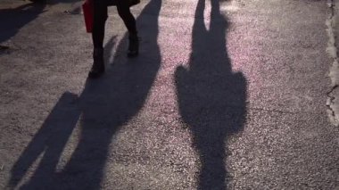 Ağır çekimde yürüyen insanların gölgeleri, alışveriş çantalı bir kadın ve iki erkek..