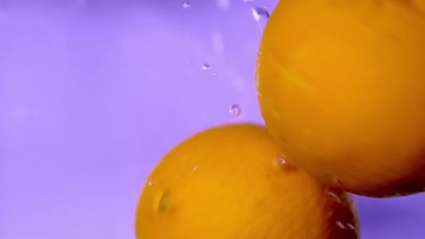 Close Slow Motion Video Oranges Dropping Spinning Water Purple Background — Stock Video