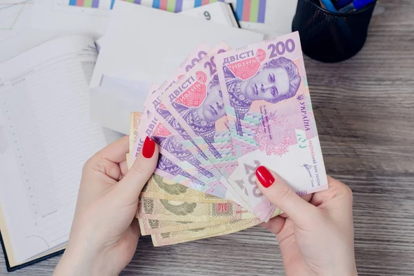 Las manos de la mujer sosteniendo dinero ucraniano sobre el escritorio — Foto de Stock