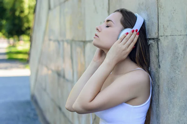 Joven chica bonita en camiseta blanca escuchando música mientras se inclina — Foto de Stock