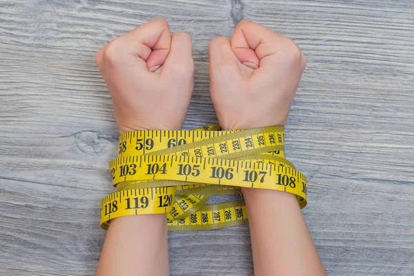 Concept of lossing weight. Woman\'s hands tied with yellow tape measure