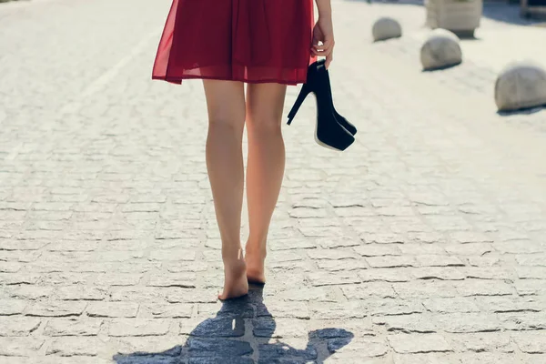 Joven hermosa dama en vestido rojo, con tacones altos negros en la mano — Foto de Stock