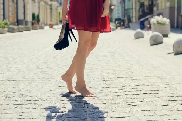Mujer en vestido elegante rojo, con zapatos de tacón alto en la mano y — Foto de Stock
