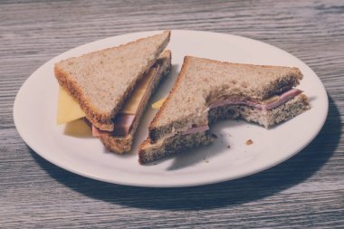 Lezzetli ısırıldı Jambonlu sandviç beyaz tabakta kapatın ahşap arka plan, yatay görünüm, vintage etkisi,