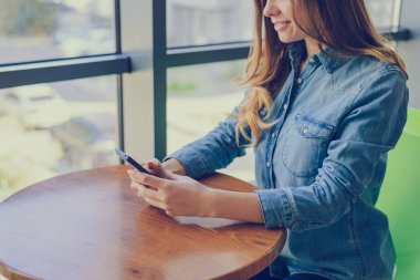 Genç güzel gülümseyen kız giyinmiş kot gömlek otururken bir