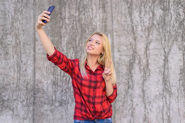 Woman in casual clothes with beaming smile taling selfie on her