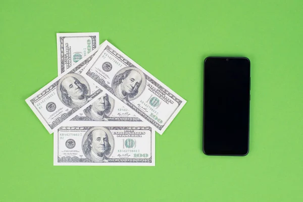 上の写真頭上のクローズアップ空のタッチスクリーンと小さな家を持つ黒いスマートフォンの携帯電話の写真アメリカのお金で作られた隔離された緑の背景 — ストック写真