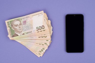 Tasarım metni ve mor arkaplan üzerine izole edilmiş Ukrayna parası yığını için boş boşluğu olan telefonun yakın plan görüntüsünün üzerinde