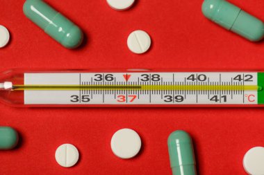 Düz zeminin üstünde düzleştirilmiş, yüksek sıcaklıkta kırmızı arkaplan üzerinde izole edilmiş termometrenin yakın plan fotoğrafı bulunuyor.