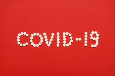 Yukarıda yukarıda, parlak kırmızı arkaplanda izole edilmiş beyaz yuvarlak haplardan yapılmış Coronavirus covid-19 yazıtlarının yakın çekim fotoğrafı var.