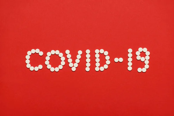上の上に近いビュー明るい赤の背景に隔離された白い丸薬で作られたコロナウイルスCovid 19の碑文の写真 — ストック写真