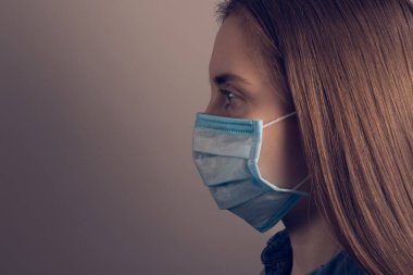 Roman koronavirüsü konsept yayıyor. Tıbbi maske takan kendine güvenen hasta bir kadının yakın plan fotoğrafı izole edilmiş gri arka plan boş alana bakıyor.