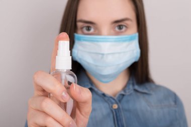 Coronavirus önleme konsepti. Gri arka planda izole edilmiş kameraya dezenfektan sıkan ciddi kendinden emin bir kızın seçici odak fotoğrafı.
