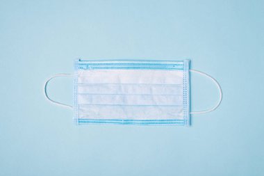 Tek kullanımlık tıbbi maske. Yukarıda mavi ve beyaz maskenin mavi arkaplanda izole edilmiş boş alandan korunması için yakın görüntü fotoğrafı.