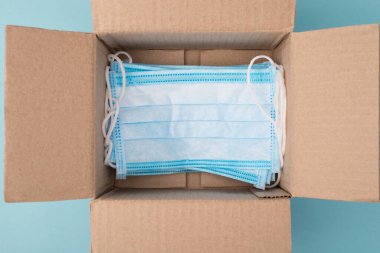 İnsani yardım konsepti. Yukarıda yukarıda, mavi arka planda bir sürü tıbbi maskesi olan paketsiz paketsiz kutunun yakın görünüm fotoğrafı var.