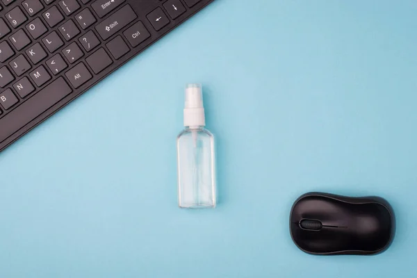 Disinfecting workplace concept. Top above overhead close up view photo of bottle with alcohol spray keyboard and computer mouse isolated on blue desk background