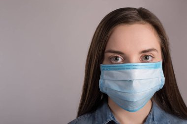 Coronavirus salgını konsepti. Yüz maskesi takan, salgına karşı korunan, gri arkaplanda bulunan ve boş alan kopyası olan bir kadının yakın plan fotoğrafı.