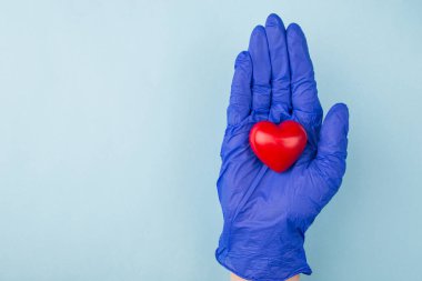 Kalp bakımı konsepti. Yukarıdaki tepede, elinde küçük kırmızı kalbi gösteren, boş boşluğu kopyalayan mavi renk arkaplanı üzerindeki el resmi kapat.