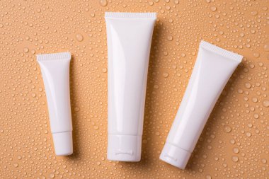 Yukarıda boş temizleyici tonik kremi için farklı boyutlardaki konteynırların resmi var. Su damlaları üzerine izole edilmiş tonik krem.