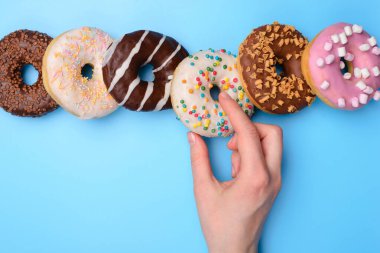 Tatlı dişli yaratıcı kavram. Yukarının üstünde, mavi pastel arka planda izole edilmiş lezzetli yuvarlak donut yiyen kadının el fotoğrafı var.
