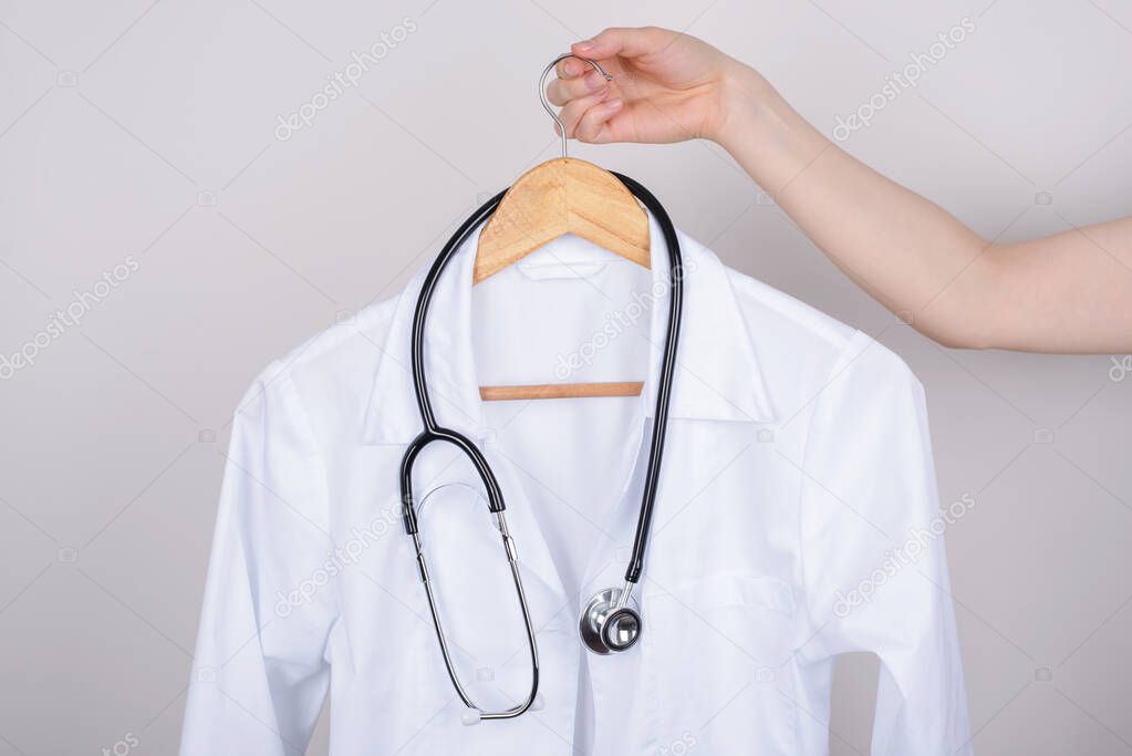 Job vacancy concept. Cropped close up photo of hand holding white doctor coat on hanger isolated over grey background