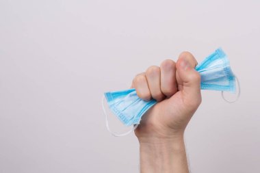 Coronavirus konseptine karşı zafer. Yakından çekilmiş bir fotoğraf. Elinde cerrahi maske tutan bir erkek. Gri arka planda izole edilmiş ve fotokopi alanı olan dar bir yumrukla.
