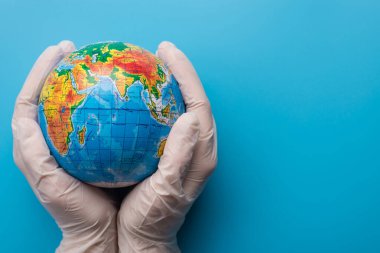 Gezegen kavramını sakla. Eldiven giyen bir insan mavi arka planda küçük bir gezegen tutar.