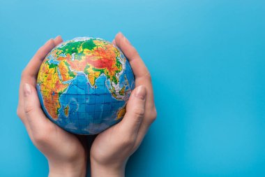 Gezegen kavramını sakla. Gezegeni mavi arkaplanda tutan bir kadının yakın plan fotoğrafı. Metin için boş kopya alanı var.