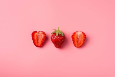 Üst tepede kesilmiş çileklerin pembe arka planda bir bütünüyle çekilmiş fotoğrafı var.