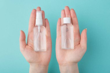 Coronavirus salgını konsepti. El dezenfeksiyonu. Yukarıdan bakıldığında, el dezenfektanlarının kadının elindeki küçük şişelerde çekilmiş fotoğrafı turkuaz arka planda izole edilmiş.