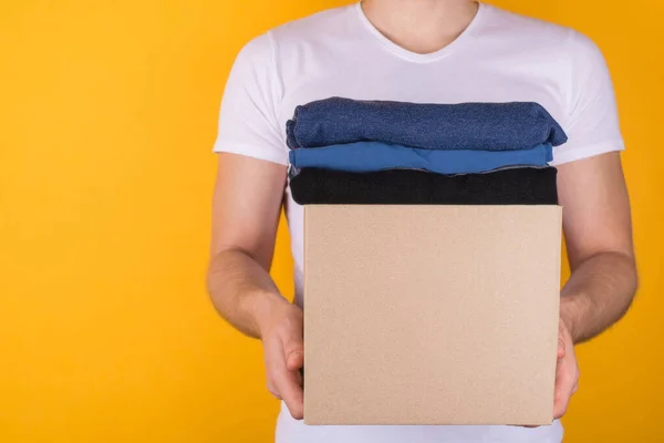 Donation concept. Cropped close up photo of man holding box full of clothes to donate isolated on yellow background